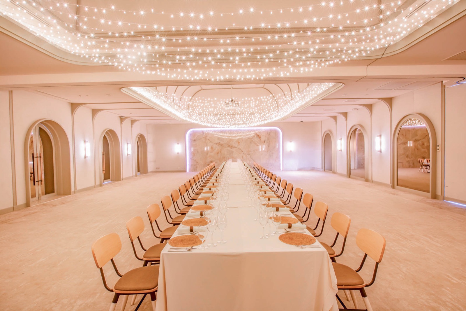 The ballroom at Centara Reserve Samui set for a wedding dinner, a canopy of fairy lights over a single long table between marble walls