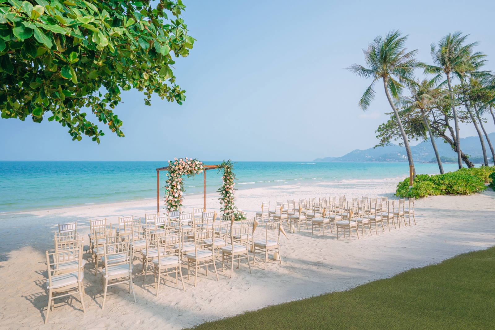 A wedding ceremony on Chaweng Beach at Centara Reserve Samui, with a floral arch, gold chairs and turquoise water behind