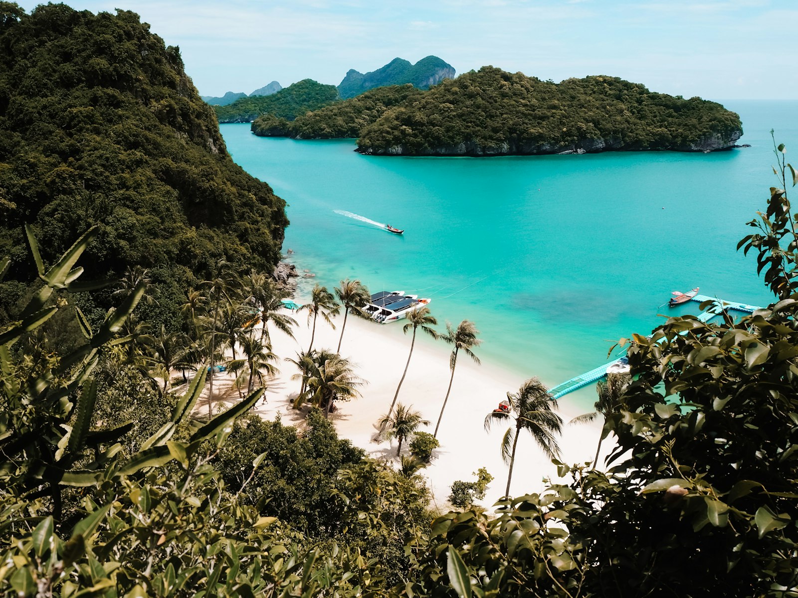 A quiet white-sand bay in the Gulf of Thailand with longtail boats in turquoise water