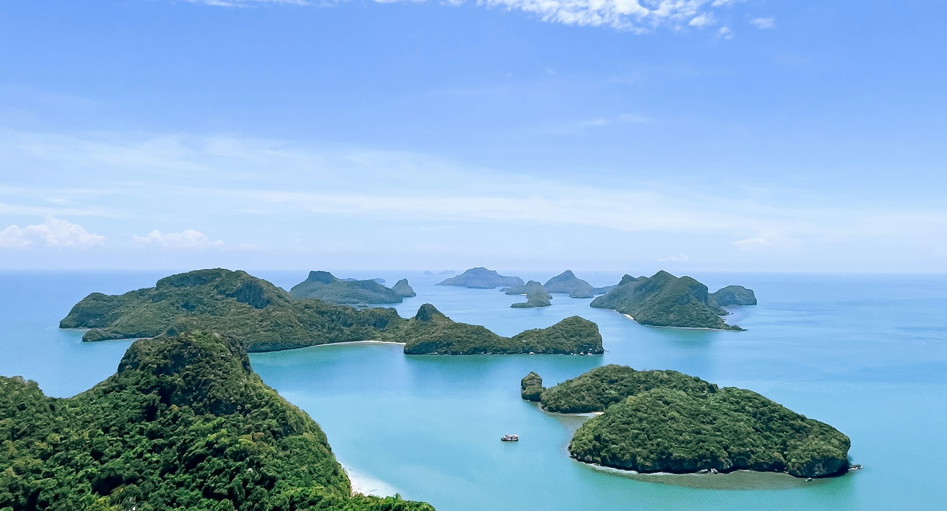 The limestone islands of Ang Thong marine park rising from a calm green sea, seen from the water on a clear day
